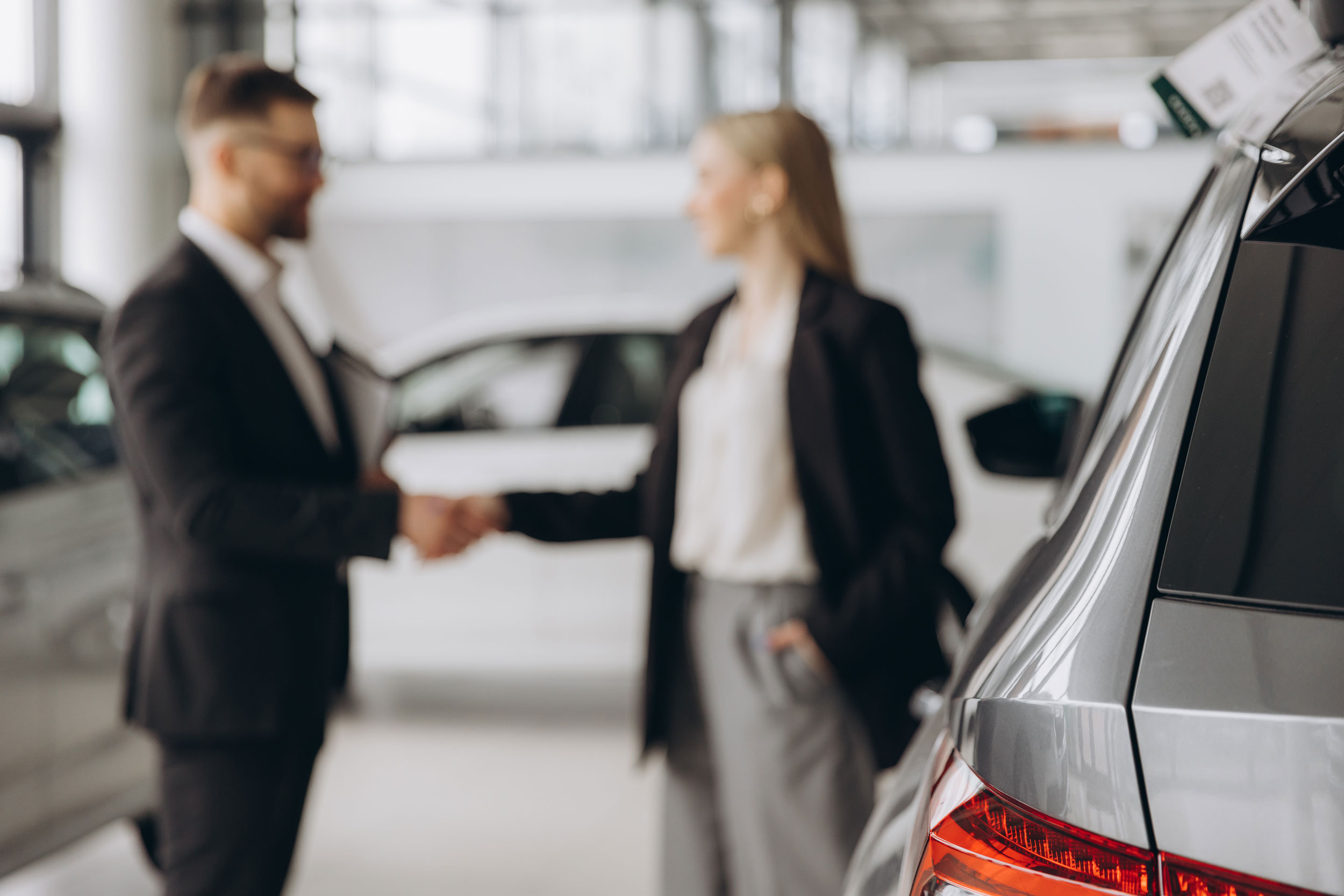 Verschwommener-Hintergrund-glückliche-Frau-kauft-ein-Auto-und-schliesst-den-Deal-mit-einem-Handschlag-mit-dem-Verkäufer